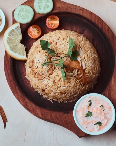 Traditional dish with rice, cashew nuts, sauce, lemon, vegetables and coriander leaf on wooden tray.